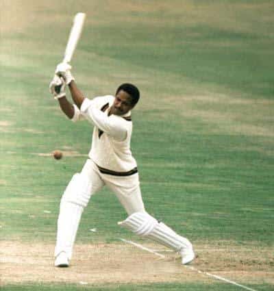 Cricketer in white batting mid swing on a cricket pitch with a ball approaching the bat